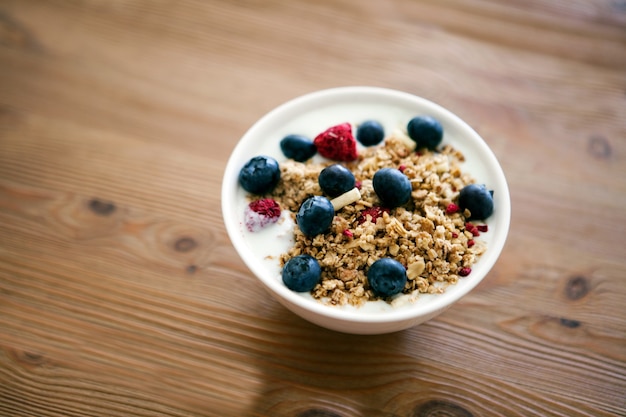 Tazón de desayuno delicioso yogur con muesli y moras frescas sobre una mesa de madera y paño de cocina de lino. Concepto de nutrición saludable y orgánica. Muesli de moras y frambuesas. Yogur en un bol