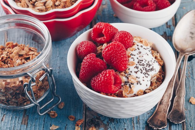 Tazón de desayuno saludable granola con yogur griego, frambuesas frescas y semillas de chía sobre fondo de madera