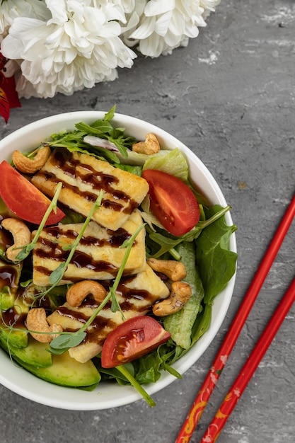 Un tazón de ensalada de pollo con palillos rojos al lado