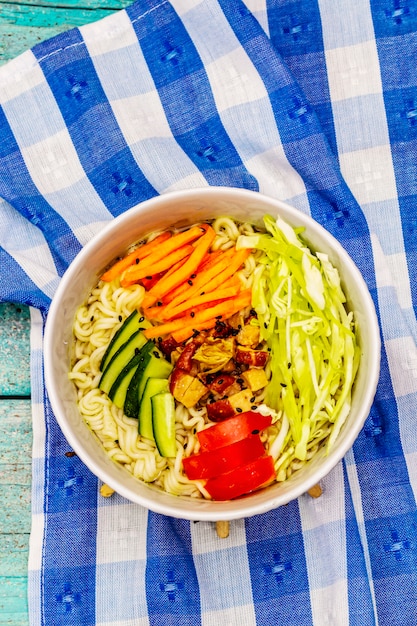 Tazón de fideos coreano tradicional con pollo ahumado, verduras frescas en rodajas y semillas de sésamo