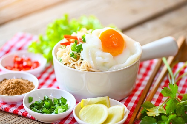 Tazón de fideos con huevo cocido vegetal cebolla tierna limón lima lechuga apio y chile en la mesa de madera comida fideos instantáneos cocinar sabroso comer con tazón de sopa de fideos