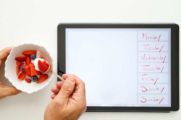 Tazón con fresas, arándanos y yogurt y tableta electrónica con los días de la semana.