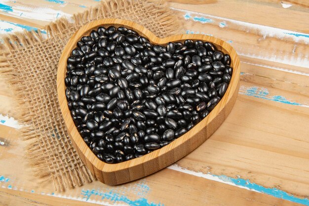 Tazón de frijol negro en forma de corazón en la mesa de madera