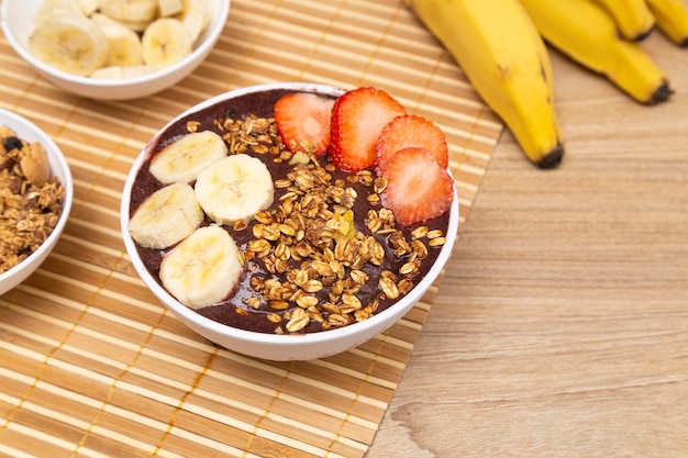 Tazón de fuente de AÃ§ai con plátano y fresa sobre mesa de madera.