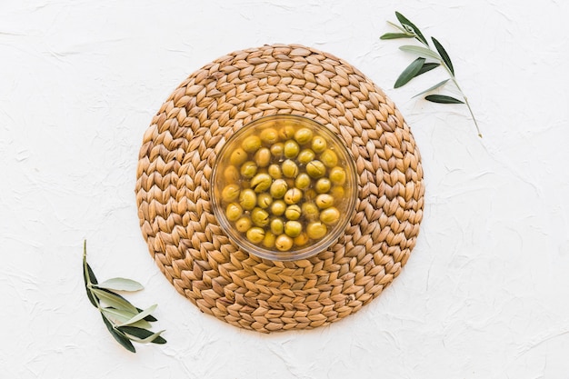 Foto tazón de fuente de aceitunas en el práctico de costa con dos ramitas sobre el fondo blanco