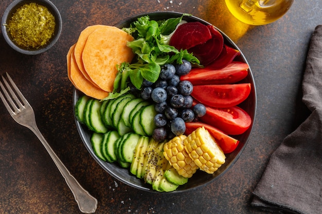 Tazón de fuente de Buda vegano con verduras y frutas servido en un tazón sobre fondo gris. De cerca