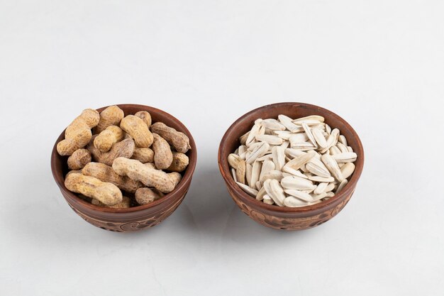 Tazón de fuente de cacahuetes orgánicos con cáscara y semillas de girasol sobre superficie blanca