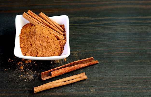 Tazón de fuente de canela en polvo con canela en rama sobre fondo de madera negra