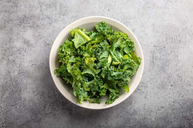 Tazón de fuente de col rizada picada verde fresca sobre fondo de piedra rústica gris, vista superior, primer plano. Ingrediente para hacer ensalada saludable. Concepto de dieta, desintoxicación o alimentación limpia