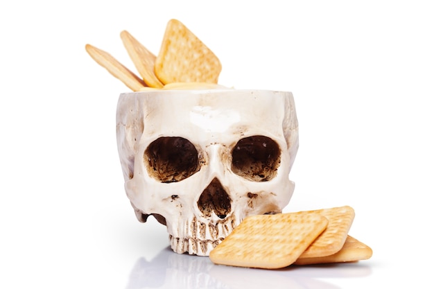 Tazón de fuente de un cráneo humano con salsa de queso y galletas aislado en blanco