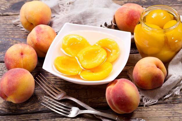 Tazón de fuente de duraznos enlatados con frutas frescas en la mesa de madera