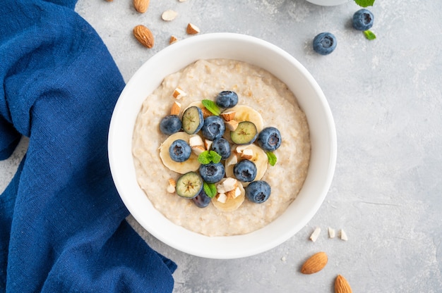 Tazón de fuente de gachas de avena con plátano, arándanos y almendras sobre un fondo de hormigón gris