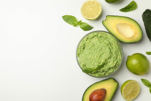 Tazón de fuente de guacamole, aguacate, lima y albahaca sobre fondo blanco, espacio para texto