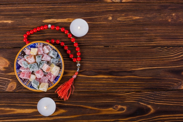 Foto tazón de fuente de lukum colorido y de rosario santo rojo con las velas encendidas en superficie de madera