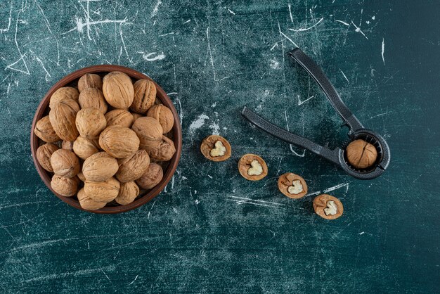 Tazón de fuente de nueces sin cáscara con herramienta para romper tuercas en la mesa de mármol.