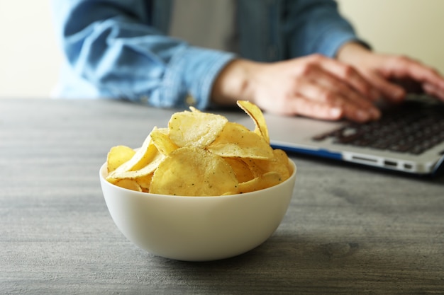 Tazón de fuente de papas fritas contra la mujer que trabaja en el portátil