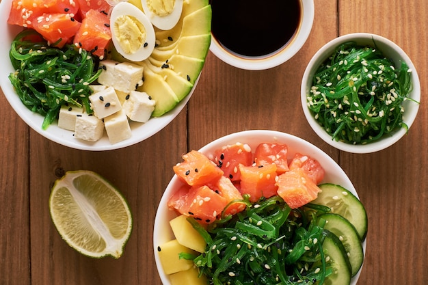 Tazón de fuente de Poke orgánico crudo con arroz, aguacate, salmón, en la vista superior de fondo de madera