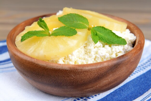 Tazón de fuente de sabroso requesón con piña en mesa de madera