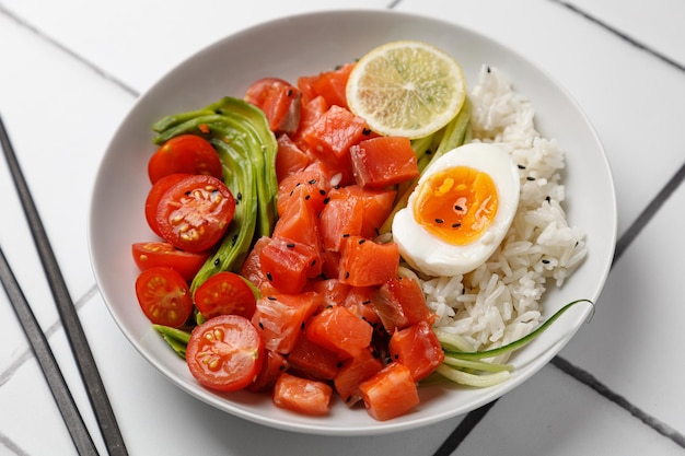 Tazón de fuente de salmón con huevo de cereza y aguacate y arroz sobre fondo de mosaico blanco con palillos