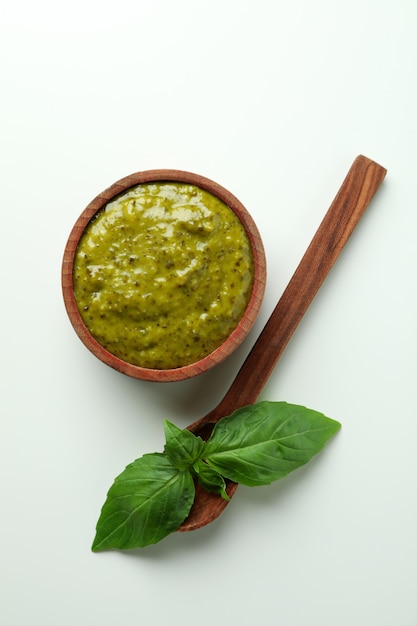 Foto tazón de fuente de salsa pesto, albahaca y cuchara sobre fondo blanco.