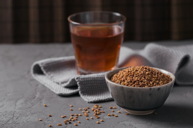 Tazón de fuente de semillas de fenogreco y té amarillo de fenogreco egipcio o bebida Methi Dana sobre fondo gris