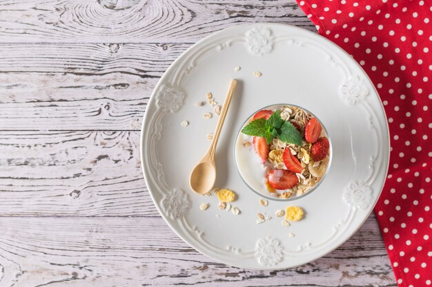 Tazón de fuente de yogur y fresas con menta y avena en una mesa de madera.