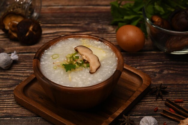 Tazón de gachas de arroz con huevo pasado por agua, rodaja de champiñón shiitake, jengibre y cebollín para el desayuno