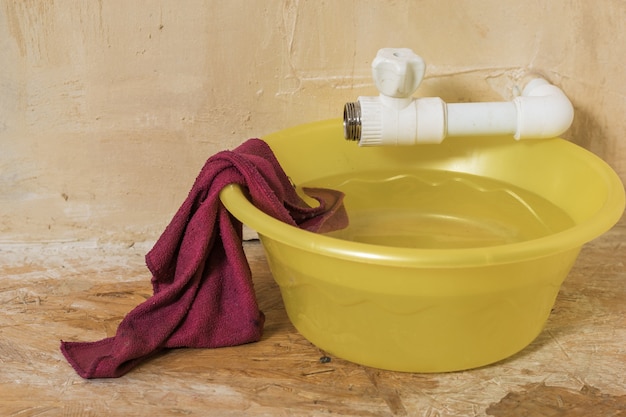 Un tazón grande de color amarillo con un paño rojo debajo de un grifo que gotea. Mal funcionamiento del sistema de suministro de agua.