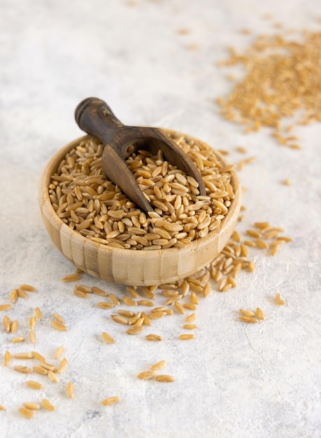 Tazón de grano de centeno seco crudo con una cuchara de madera en la mesa blanca de cerca