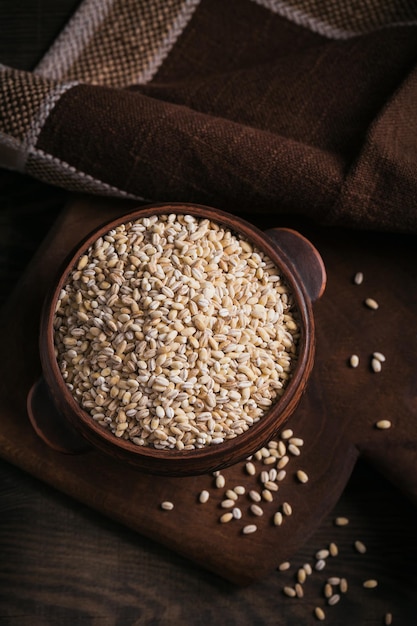 Tazón de grano de cereal de cebada perlada rota cruda seca sobre fondo de madera oscura Concepto de gachas de cebada perlada para cocinar