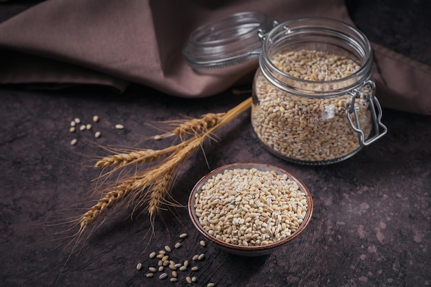 Tazón de grano de cereal de cebada perlada roto crudo seco sobre fondo oscuro Concepto de gachas de cebada perlada para cocinar