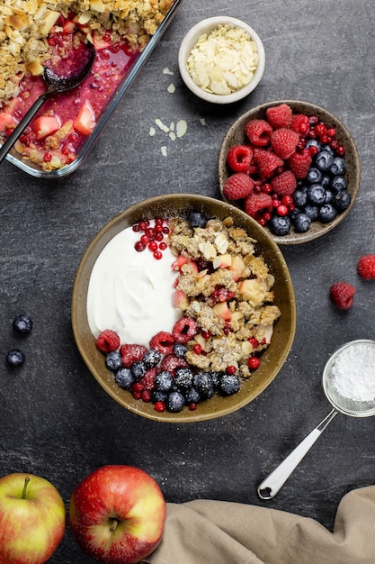 Tazón de granola casera con yogur y bayas frescas sobre hormigón de piedra oscura.