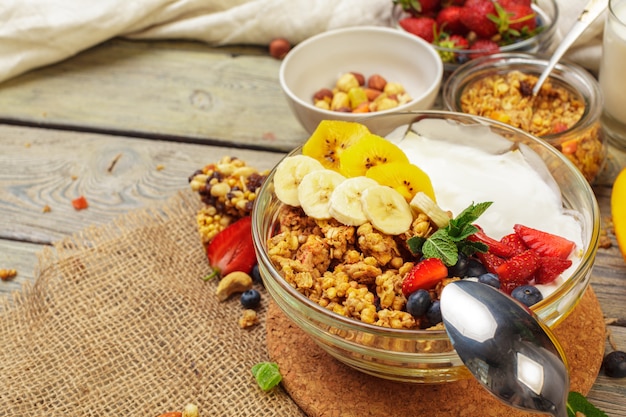 Tazón de granola casera con yogur y bayas frescas sobre superficie de madera