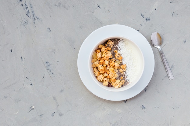 Tazón de granola casera con yogur y semillas de chía en la superficie de piedra desde la vista superior. Hora del desayuno