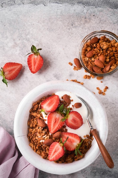 Tazón de granola de granola casera con yogur y bayas frescas de fresa para el desayuno en un tazón blanco sobre fondo de mesa de fondo de hormigón gris antiguo Vista superior fondo plano