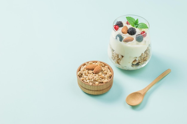 Un tazón de granola y un vaso de yogur y bayas sobre un fondo azul.