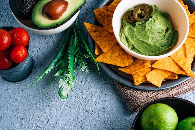 Tazón con guacamole mexicano en mesa de madera vintage, rodeado de tomates, jalapeños, limas y aguacates. Copyspace