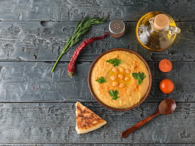 Tazón con hummus fresco, aceite de oliva, chile y tomates cherry sobre una mesa rústica oscura