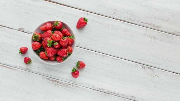 Un tazón de jugosas fresas rojas sobre la mesa de madera blanca. Concepto de bocadillos saludables y dietéticos.