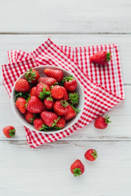 Un tazón de jugosas fresas rojas sobre la mesa de madera blanca. Concepto de bocadillos saludables y dietéticos.