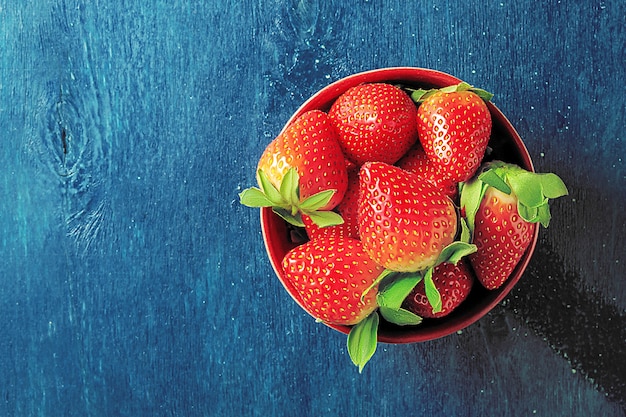 Un tazón de jugosas fresas sobre un fondo azul oscuro con espacio de copia.