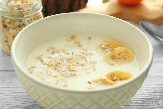 Tazón con leche de avena y rodajas de plátano para el desayuno en la mesa de madera