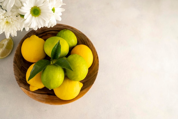 Tazón con limas y limones frescos sobre fondo de madera Frutas cítricas frescas con espacio de copia de flores frescas