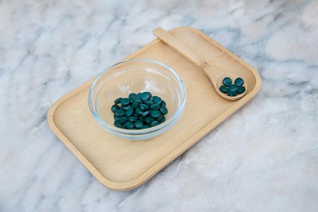 Un tazón de pastillas verdes en una bandeja de madera con una cuchara a un lado.