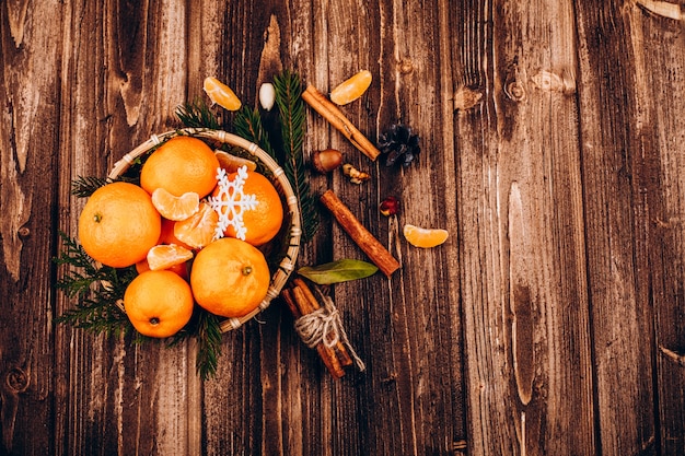 Tazón con pequeñas mandarinas se encuentra en la mesa de madera con especies para bebidas navideñas