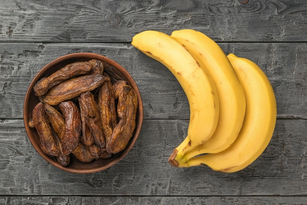 Un tazón de plátanos secos y tres plátanos maduros sobre una mesa de madera Delicioso bocadillo de frutas naturales Lay Flat