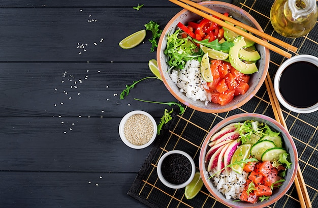 Foto tazón de poké de salmón hawaiano con arroz, aguacate, pimentón, pepino, rábano, semillas de sésamo y lima.