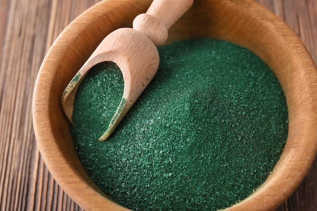 Tazón con polvo de espirulina y cuchara sobre fondo de madera