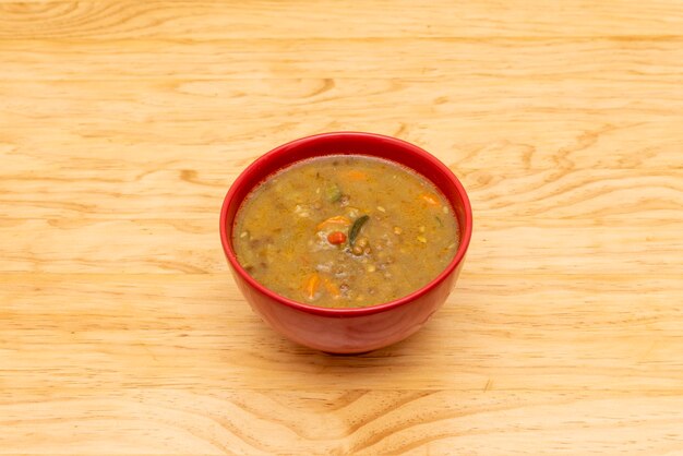 Tazón rojo con estofado de frijoles veganos tostados en una mesa de madera clara