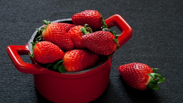 un tazón rojo de fresas con una olla roja en el lado